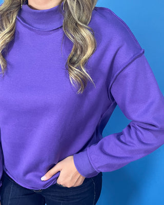 Purple long sleeve mock neck sweatshirt top with a relaxed fit and raw edge details.