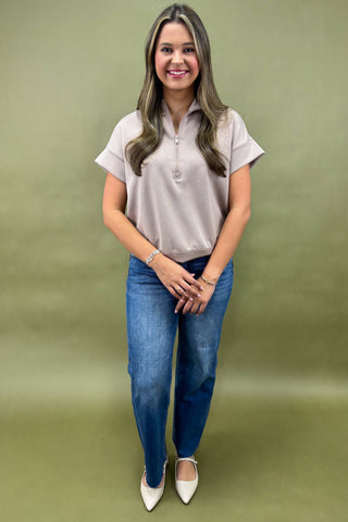 Woman wearing a light gray polo shirt and blue jeans against a green background