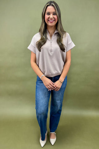 Woman wearing a light gray polo shirt and blue jeans against a green background
