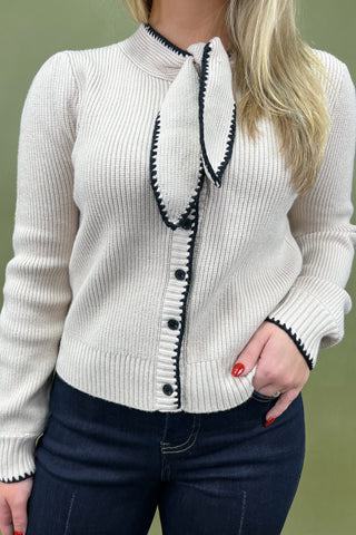 White ribbed sweater with black trim worn by a person against a green background