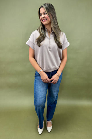 Woman wearing a light gray polo shirt and blue jeans against a green background