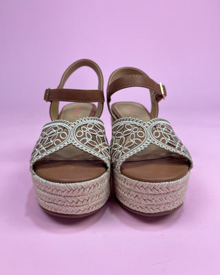 Pair of open-toe sandals with woven sole and decorative straps on a pink background