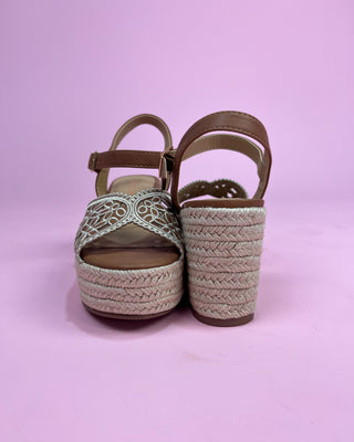 Pair of green wedge sandals with braided sole on a pink background