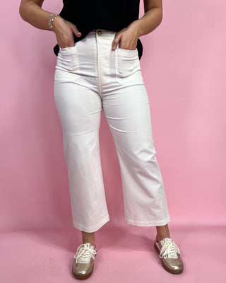 Person wearing white jeans and brown shoes on a pink background