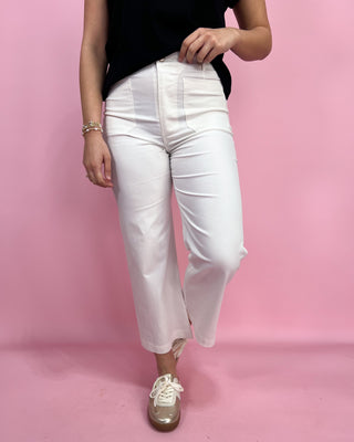Person wearing white pants and a black top on a pink background