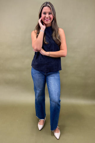 Woman wearing a navy sleeveless top and blue jeans against a beige background