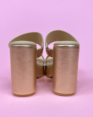 Pair of gold high-heeled shoes on a pink background