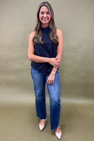 Woman wearing a navy sleeveless top and blue jeans against a beige background