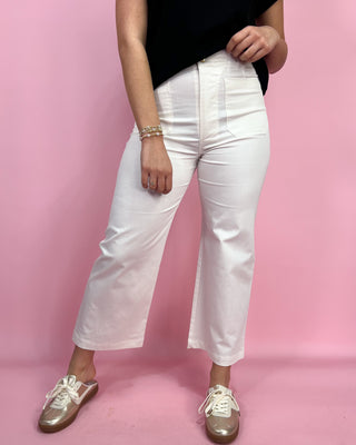 Person wearing white pants and black top on a pink background
