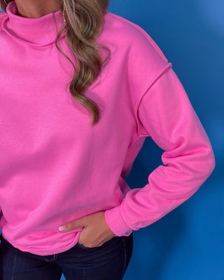 Hot pink long sleeve mock neck sweatshirt top with raw edge details and a relaxed fit.