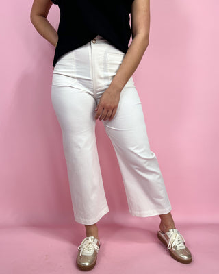 Person wearing white pants and black top on a pink background