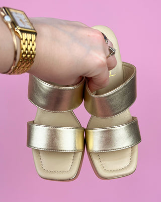 Gold sandals being worn with a pink background