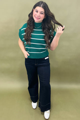 Woman wearing a green and white striped sweater with black pants on a beige background