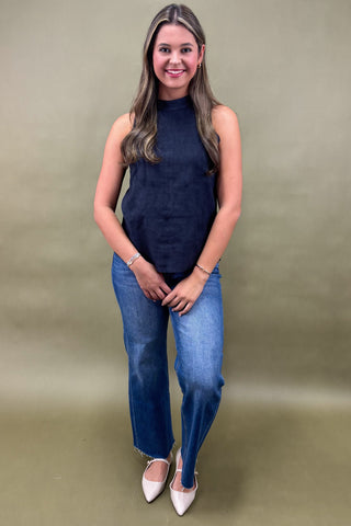 Woman wearing a navy sleeveless top and blue jeans against a beige background