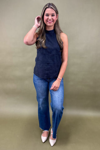 Woman wearing a navy sleeveless top and blue jeans against a beige background