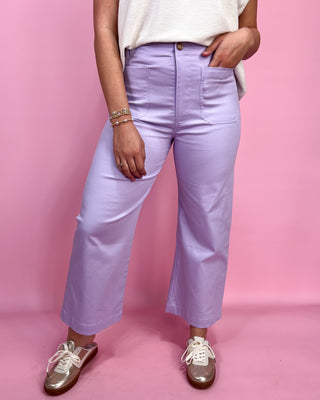 Person wearing light purple pants and white sneakers on a pink background