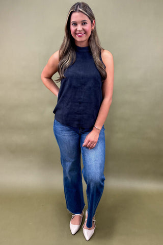 Woman wearing a navy sleeveless top and blue jeans against a green background