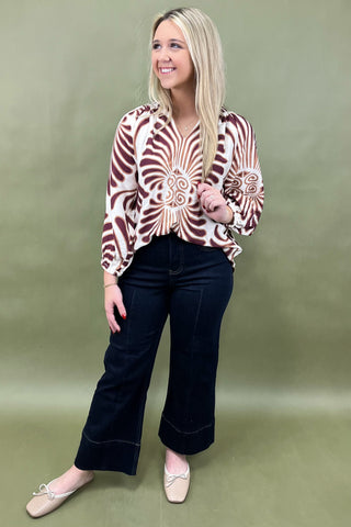 Woman wearing a patterned blouse and black pants against a green background