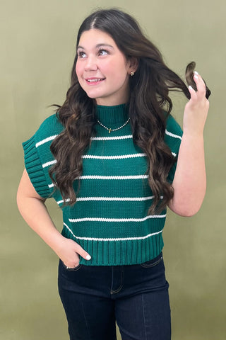 Woman wearing a green sleeveless sweater with white stripes against a beige background