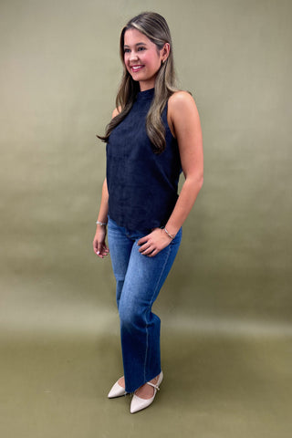 Woman wearing a navy sleeveless top and blue jeans against a green background