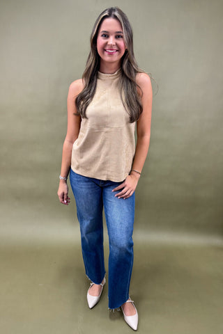Woman wearing a beige sleeveless top and blue jeans against a plain background