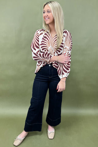 Woman wearing a patterned blouse and dark pants on a green background