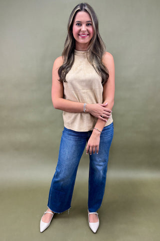 Woman wearing a beige sleeveless top and blue jeans against a green background