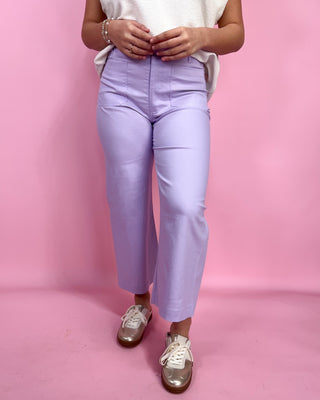 Person wearing light purple pants and white sneakers on a pink background