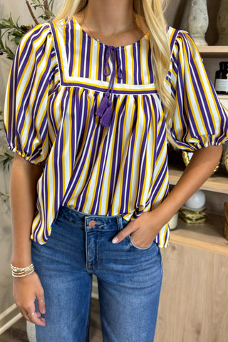 Woman wearing a purple and yellow striped blouse with blue jeans indoors.