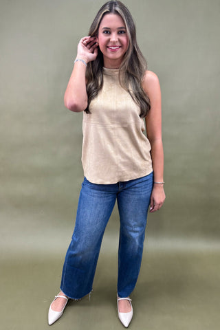Woman wearing a beige sleeveless top and blue jeans against a green background