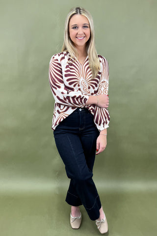 Woman wearing a patterned blouse and black pants against a green background