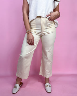 Person wearing white pants and a white top on a pink background