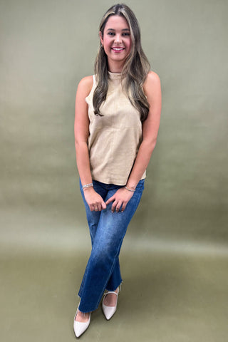 Woman wearing a beige sleeveless top and blue jeans against a plain background