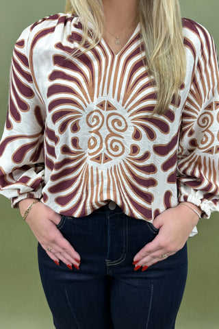 Person wearing a patterned blouse with long sleeves on a green background