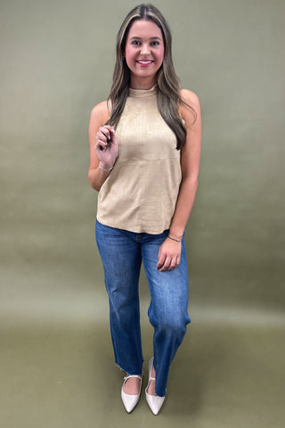 Woman wearing a beige sleeveless top and blue jeans against a plain background