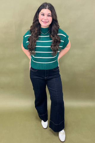 Woman wearing a green striped sweater and dark jeans against a beige background