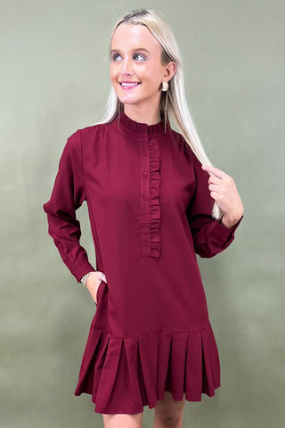 Woman wearing a burgundy dress with a ruffled neckline and hem against a green background