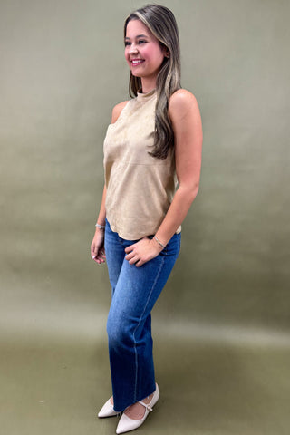Woman wearing a beige sleeveless top and blue jeans against a plain background