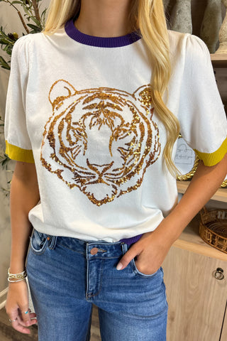 Person wearing a white t-shirt with a gold tiger design and blue jeans indoors.