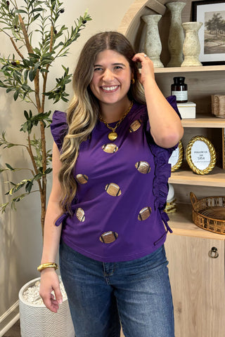 Woman wearing a purple top with gold embellishments in a home setting.