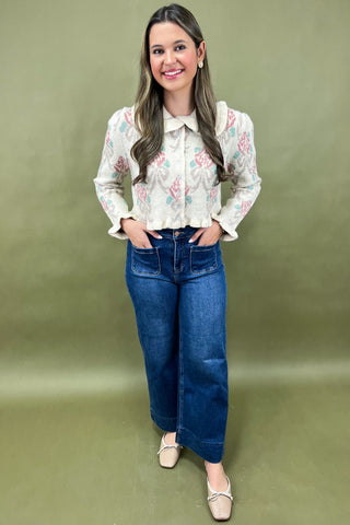 Woman wearing a floral blouse and blue jeans against a green background