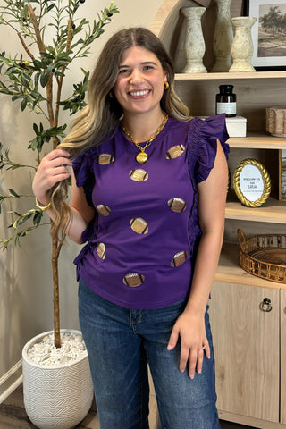 Woman wearing a purple top with gold embellishments in a home setting.