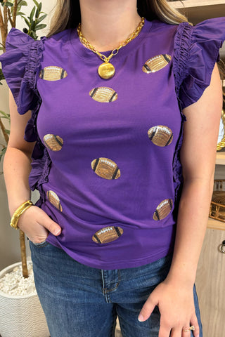 Person wearing a purple top with football patterns and gold jewelry indoors.