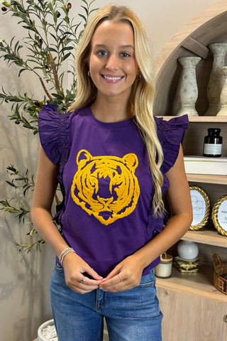 Woman wearing a purple shirt with a yellow tiger logo in a home setting.