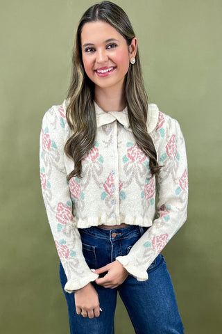 Woman wearing a white floral blouse and blue jeans against a green background