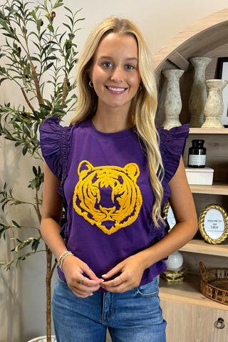 Woman wearing a purple shirt with a yellow tiger logo in a home setting.