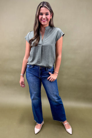 Woman wearing a green top and blue jeans against a beige background