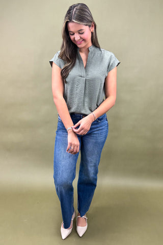 Woman wearing a green top and blue jeans against a beige background