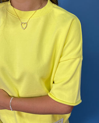 A woman modeling a Lulu Mac bright yellow oversized short-sleeve t-shirt and matching yellow shorts against a solid blue studio backdrop.