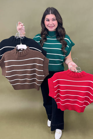 Woman holding three striped sweaters against a plain background
